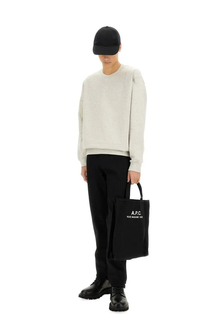 Black canvas tote bag with white a.p.c. logo displayed with a grey a.p.c. men’s sweatshirt in the background