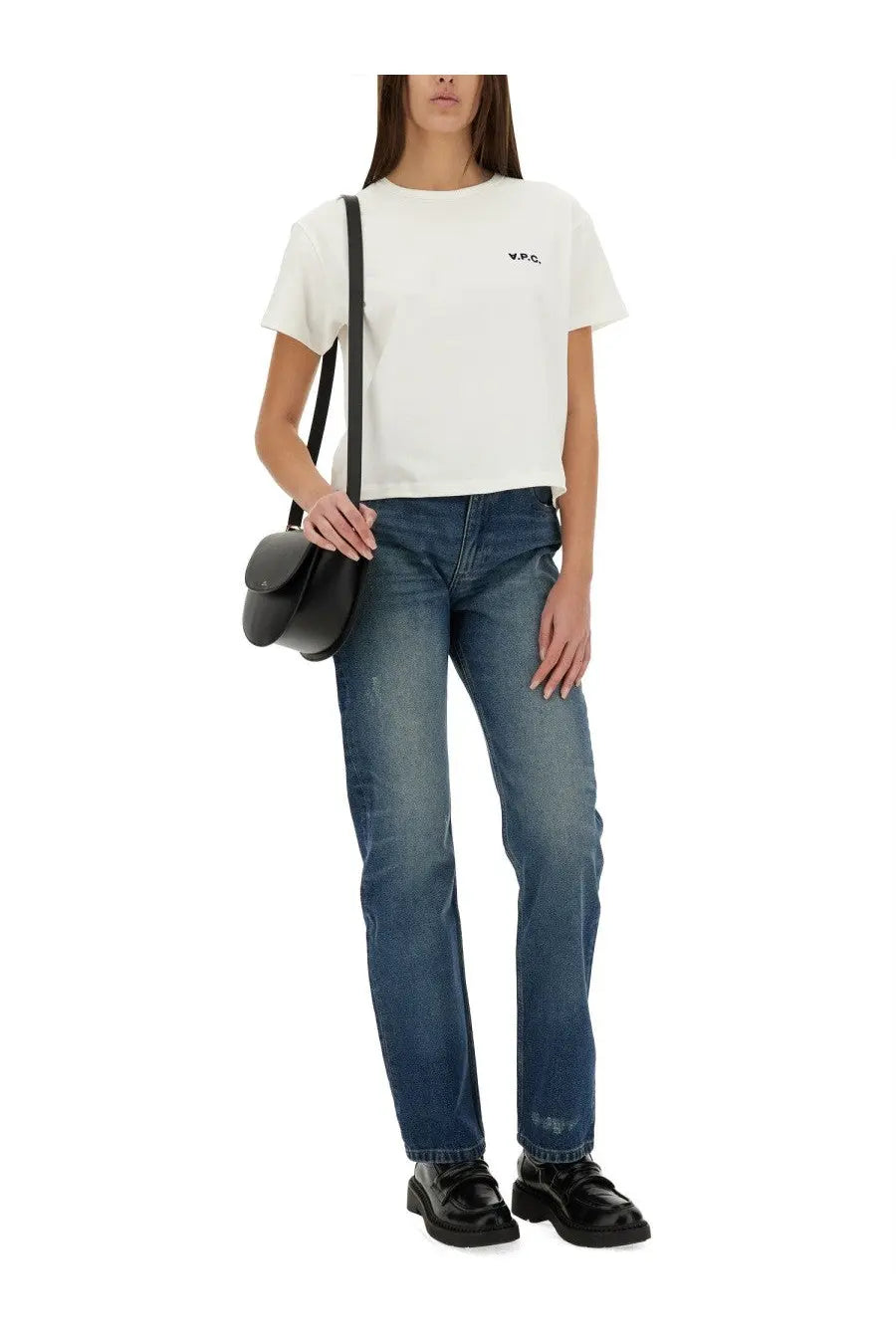 Black leather crossbody bag with minimalist design and rounded flap closure alongside A.P.C women’s kylie blue jeans
