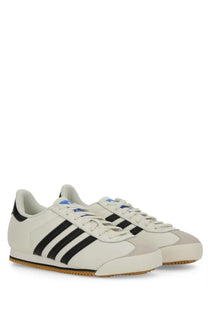 Cream-colored adidas men’s kick sneaker with black three stripes and gum rubber sole for casual wear