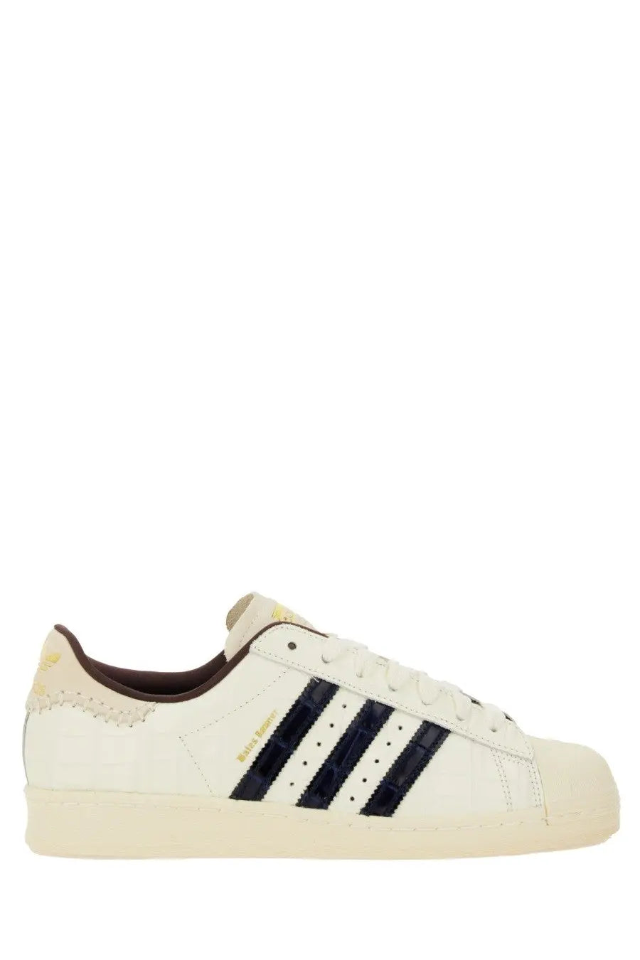Cream-colored adidas Originals Superstar sneaker with navy blue stripes and brown heel tab by Wales Bonner