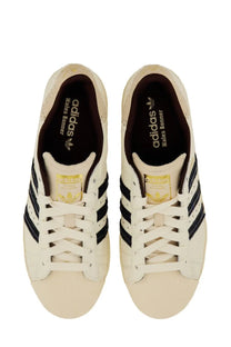 Cream-colored adidas Originals by Wales Bonner men’s sneaker Superstar with black three-stripe stripes and gold branding accents