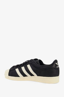 Black adidas originals x willy chavarria men’s leather superstar sneaker with three white stripes and cream rubber toe cap