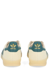 Back view of cream-colored adidas unisex gazelle indoor sneaker with teal accents and gold branding on the heel