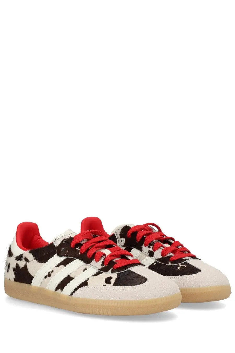 Adidas unisex Samba OG sneaker with white and black cow print, red laces, and tan rubber sole in multicolor