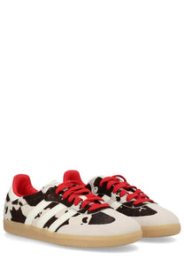 Adidas unisex Samba OG sneaker with white and black cow print, red laces, and tan rubber sole in multicolor