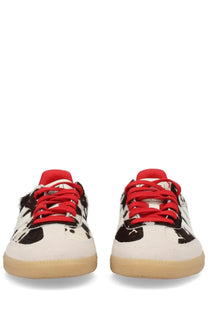 Adidas unisex Samba OG sneaker with white black cow print, red laces and tongue, and tan rubber sole