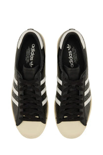 Black adidas unisex superstar vintage sneaker with white three stripes and cream rubber toe cap in leather
