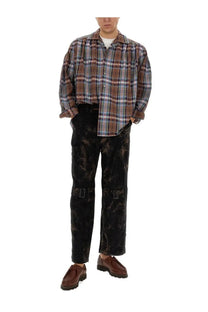 A man wearing a brown blue and white plaid shirt with aïe men’s black ribbed distressed pants