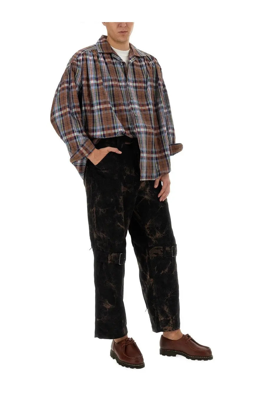 A man wearing an AïE men’s seersucker cotton shirt blue with loose-fitting plaid design over black tie-dye cargo pants