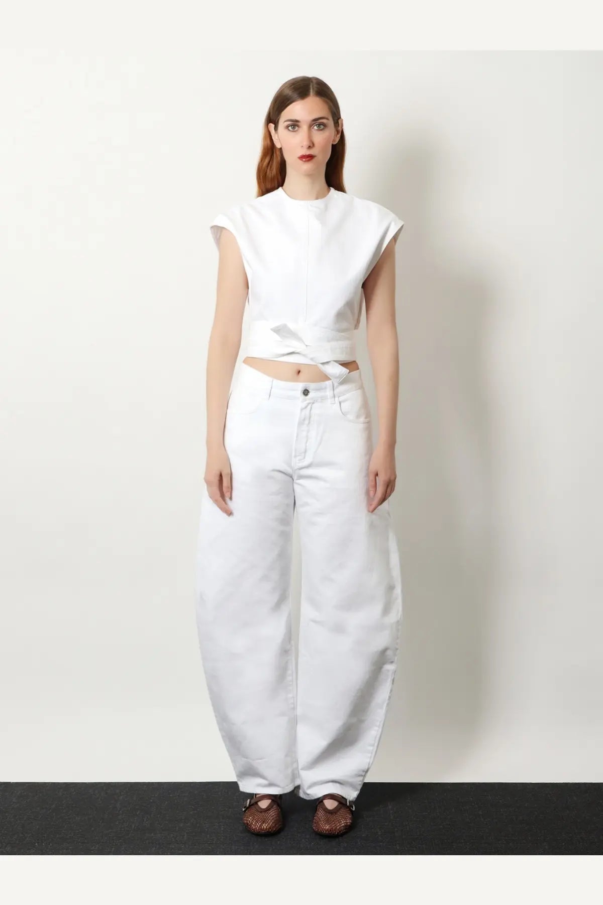 White sleeveless cropped top with front tie detail paired with ALAÏA women’s curved white denim trousers