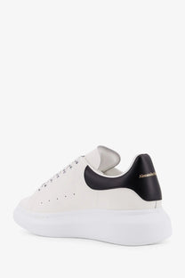 Alexander McQueen men’s low top white leather sneakers with black heel tab and gold branding visible from back side