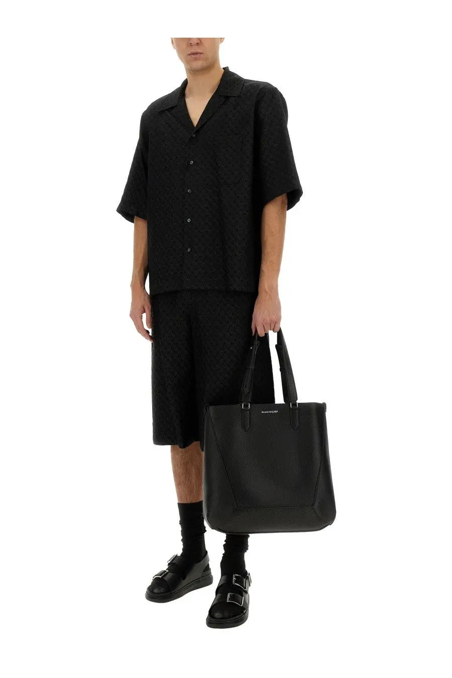 Black leather tote bag with structured design and top handles paired with Alexander McQueen skull pattern shirt black