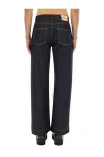 Dark indigo Alexander McQueen men’s wide leg denim jeans with white stitching and branded leather patch at waistband back view