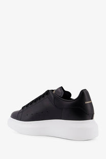 Back view of black leather alexander mcqueen women’s oversized sneakers with thick white sole and gold heel branding