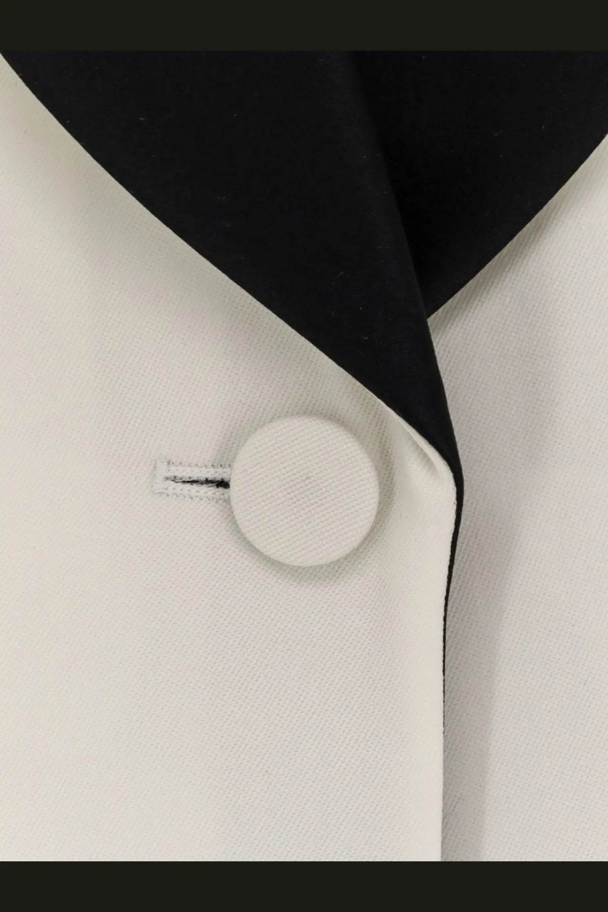 White circular button with textured surface on alexander mcqueen women’s white wool blazer against black and white fabric