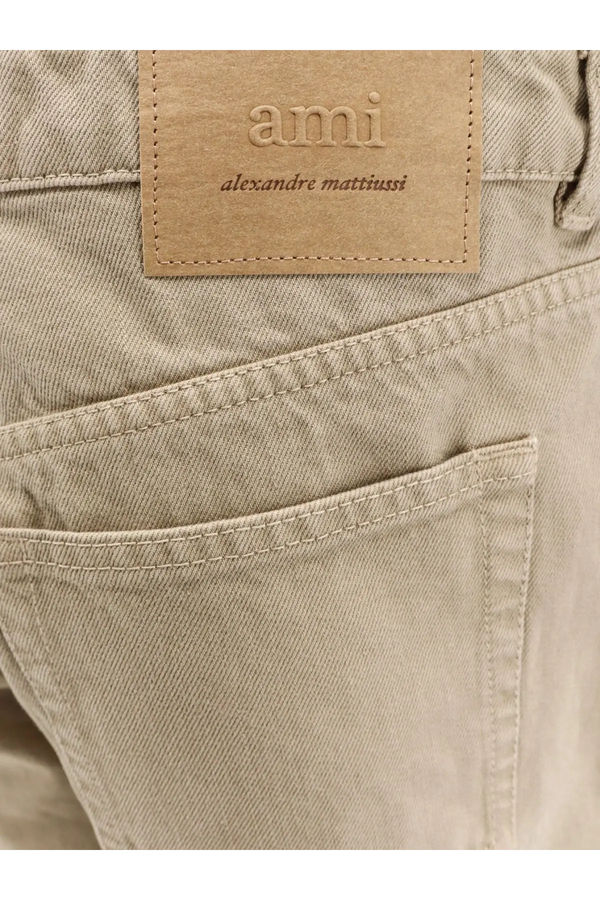 Beige denim Ami Paris men’s cotton trousers with tan leather brand patch embossed ami alexandre mattiussi on back