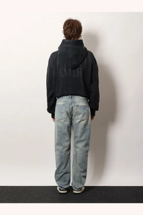 Back of a black cropped hoodie with subtle embossed lettering paired with amiri men’s destroyed effect jeans blue