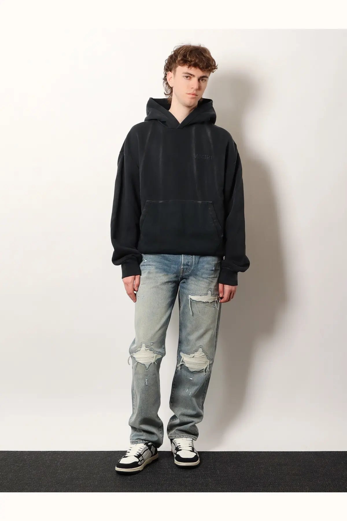 Black oversized hoodie with subtle chest logo and ribbed cuffs paired with amiri men’s destroyed effect blue jeans