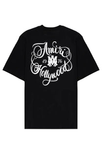Black amiri men’s hollywood t-shirt with bold white cursive amiri hollywood 1976 graphic and interlocking m logo