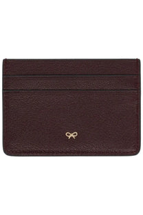 Anya Hindmarch women’s burgundy leather card holder with pebbled texture and gold bow emblem at bottom center