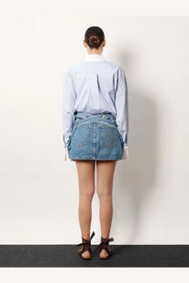 The Attico women’s denim skirt blue paired with a blue and white vertically striped long-sleeved button-up shirt