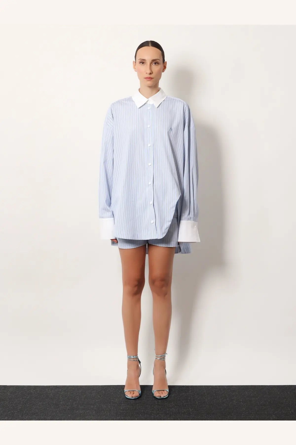A woman wearing the attico women’s oversize striped cotton shirt in white with blue stripes and a white collar and cuffs