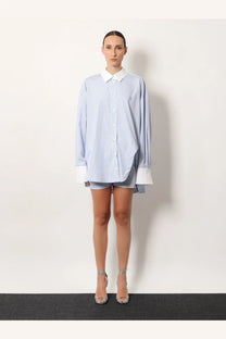 A woman wearing the attico women’s oversize striped cotton shirt in white with blue stripes and a white collar and cuffs