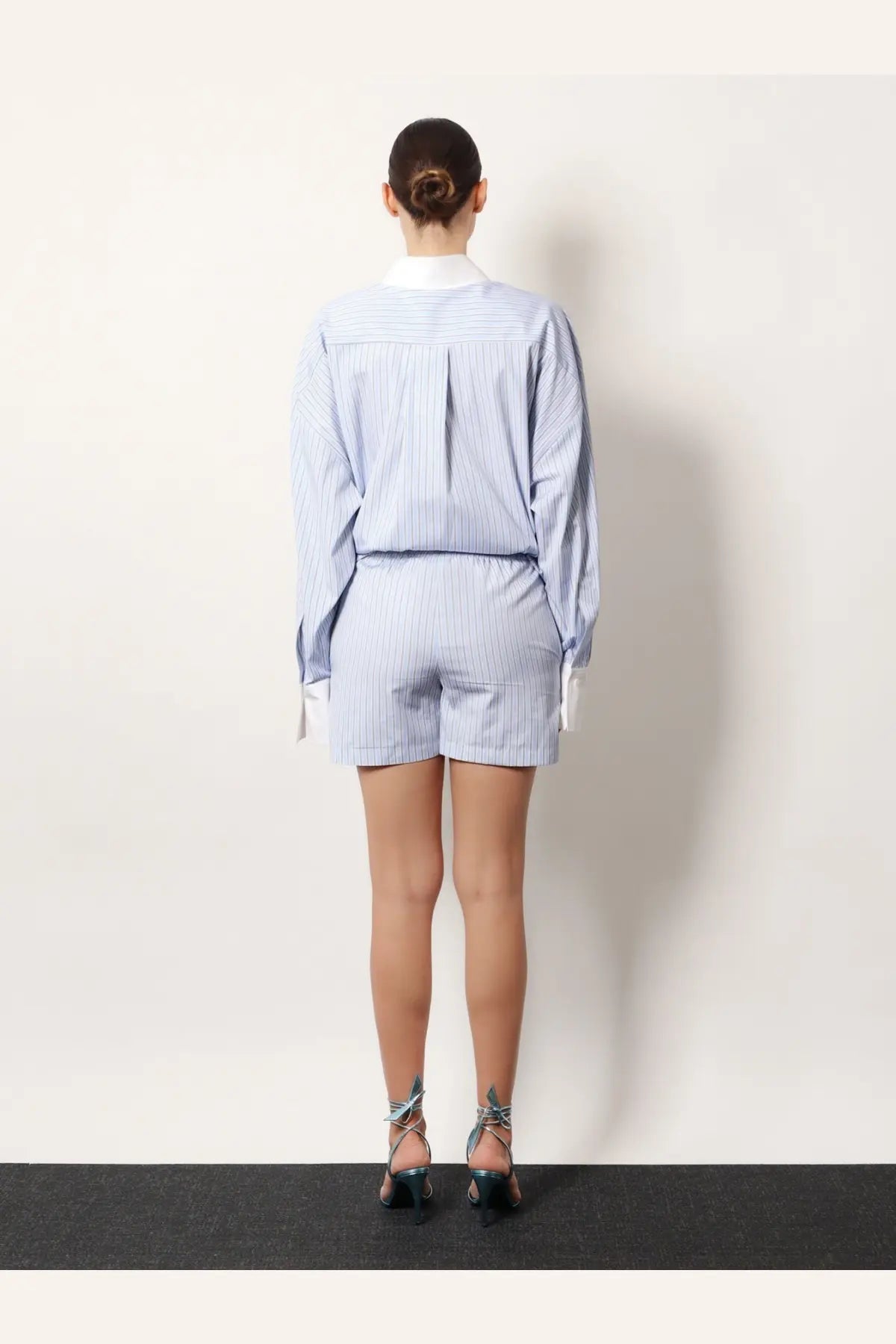 A woman wears the Attico women’s white striped cotton shorts with a matching light blue and white striped long-sleeved shirt