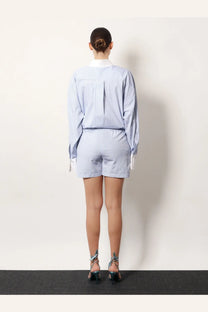 A woman wears the Attico women’s white striped cotton shorts with a matching light blue and white striped long-sleeved shirt