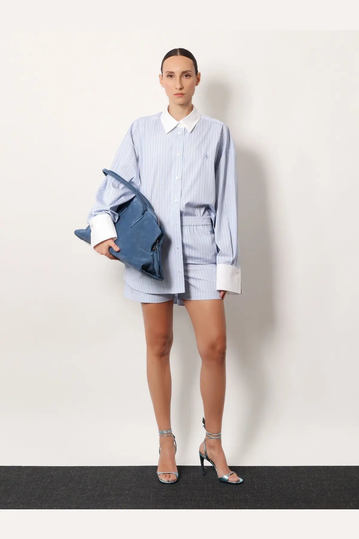 A woman wearing the attico women’s striped cotton shorts white paired with a long-sleeved blue and white striped shirt with white cuffs and collar