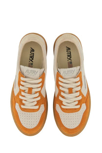 Autry women’s medalist low sneaker in orange and white suede and leather with gum rubber sole visible from front angle