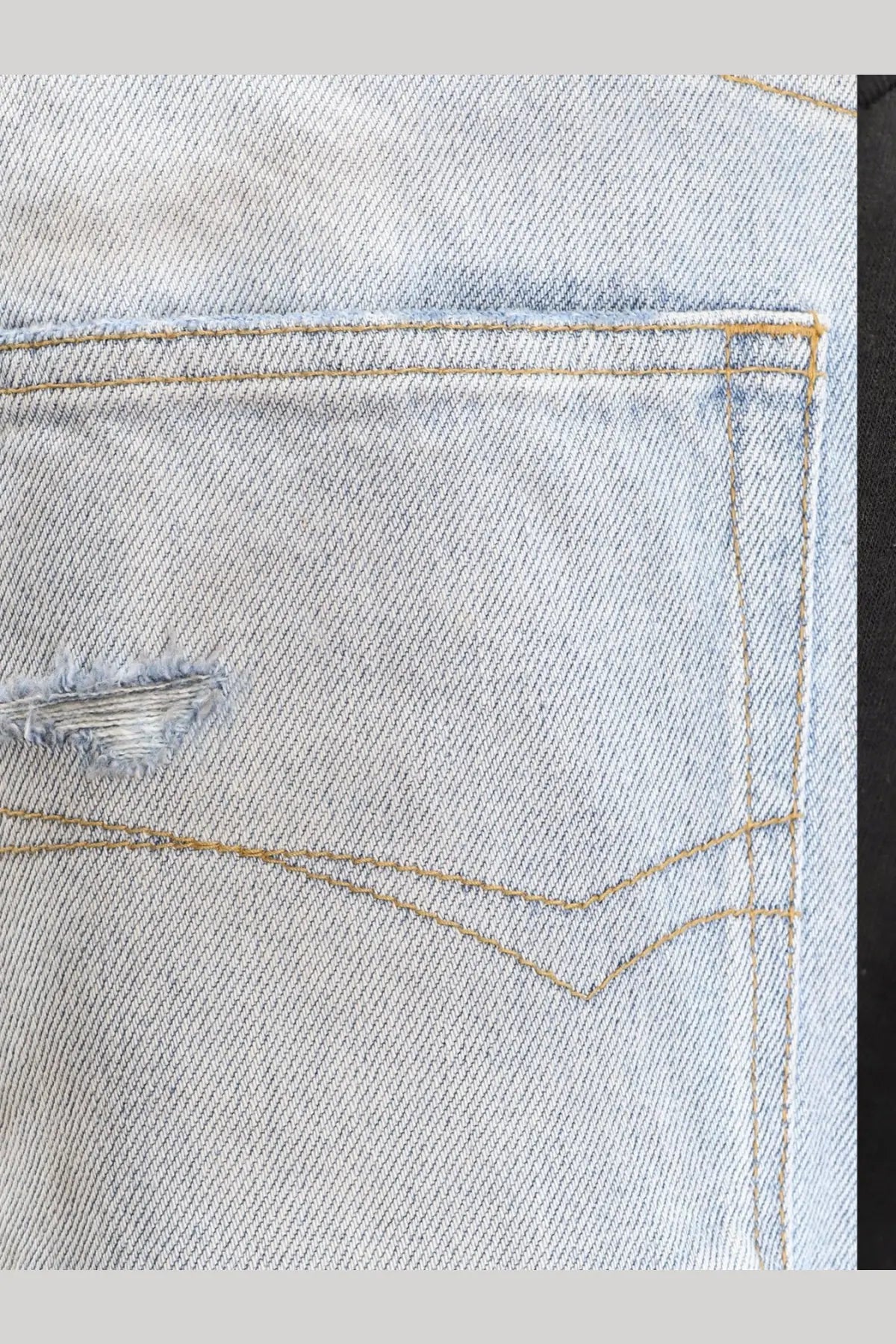 Balenciaga men’s distressed light-wash denim jeans back pocket with frayed tear and tan contrast stitching