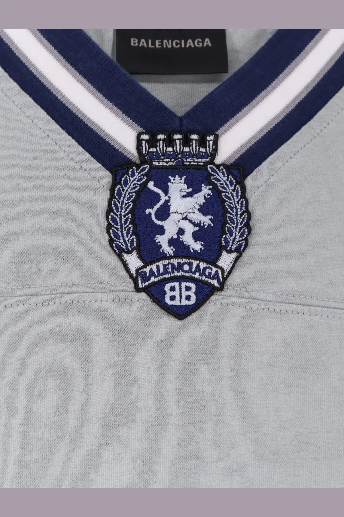 Balenciaga men’s football jersey shirt grey with v-neck sweater design and navy blue crest embroidered with white lion and laurel wreath