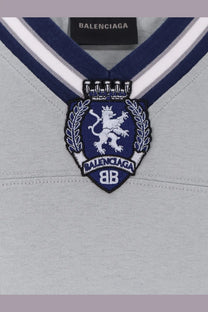 Balenciaga men’s football jersey shirt grey with v-neck sweater design and navy blue crest embroidered with white lion and laurel wreath