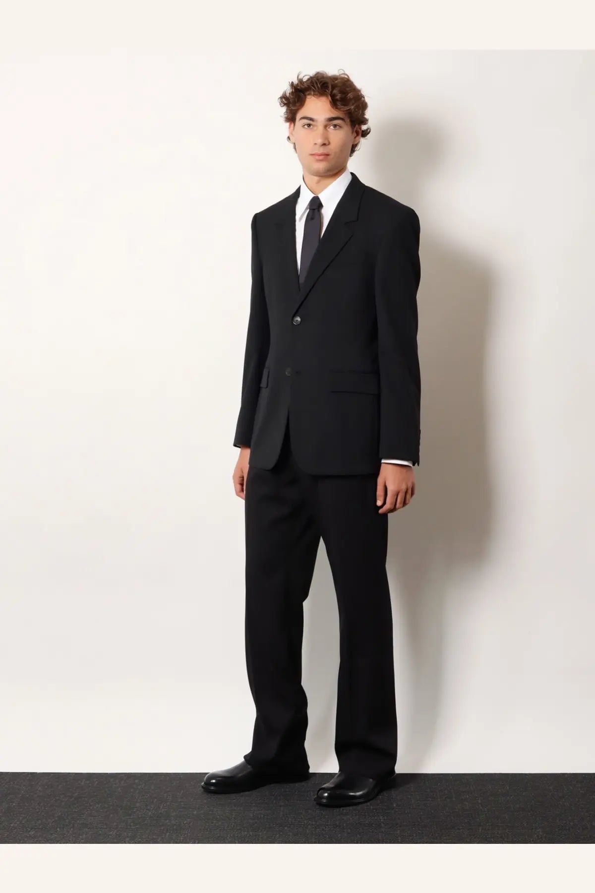 Balenciaga men’s straight fit black cotton trousers paired with a black single-button suit jacket white shirt and dark tie