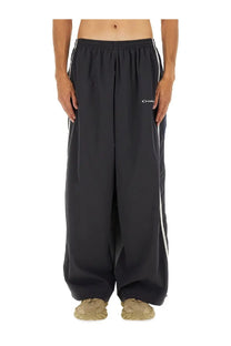 Balenciaga men’s black wide-leg track pants with white side stripes and small embroidered logo on the left thigh