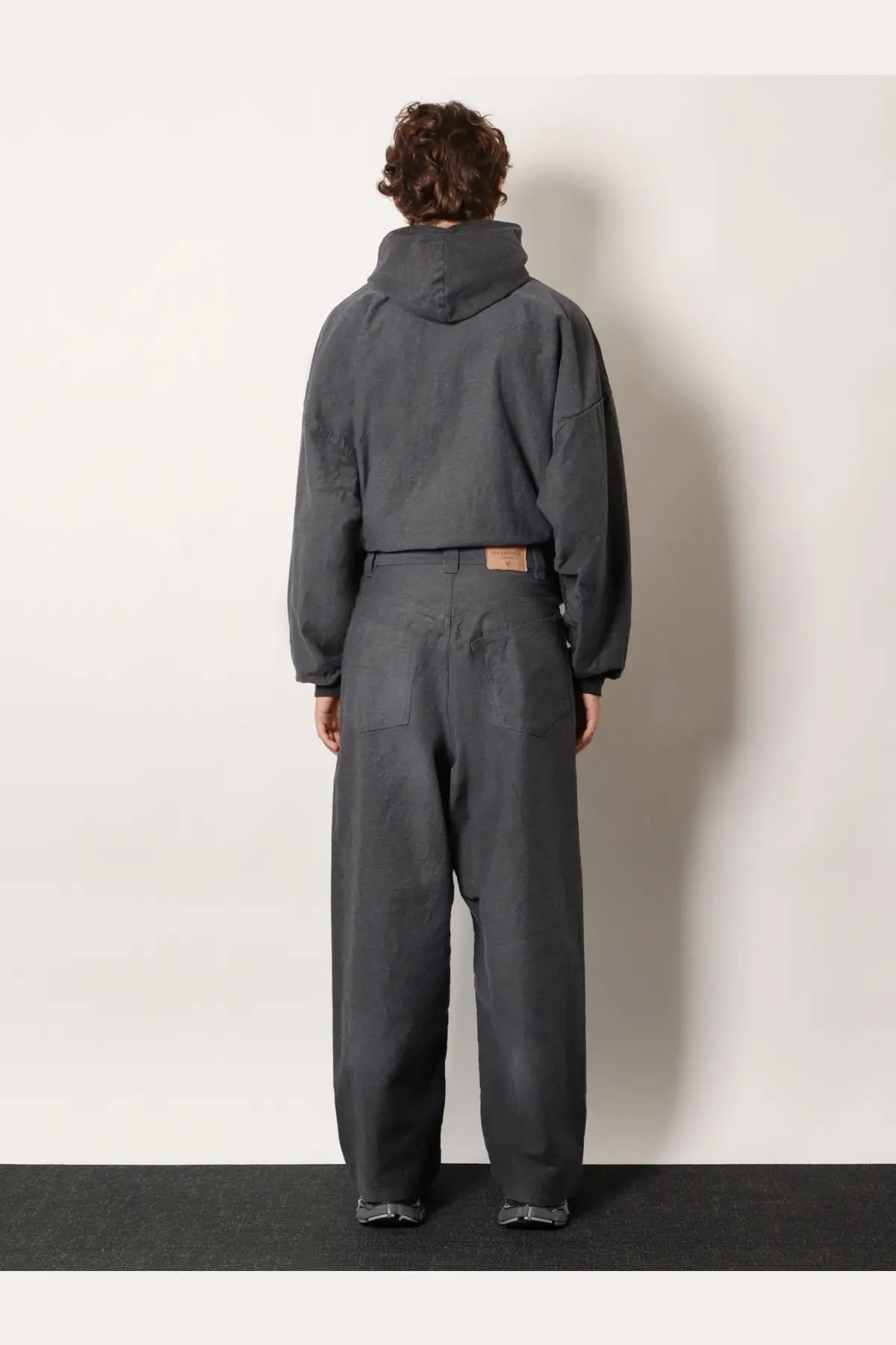Dark gray hooded jacket with relaxed oversized fit and subtle stitching paired with balenciaga men’s trompe loeil denim trousers white