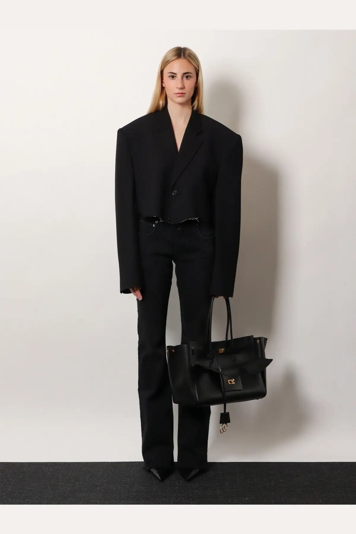 Black leather tote bag with gold-tone hardware and bow detail styled with Balenciaga women’s black denim trousers