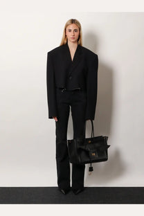 Black leather tote bag with gold-tone hardware and bow detail styled with Balenciaga women’s black denim trousers