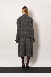 A woman wears a balenciaga women’s one layer raglan wool coat black in gray and black plaid with a belted waist