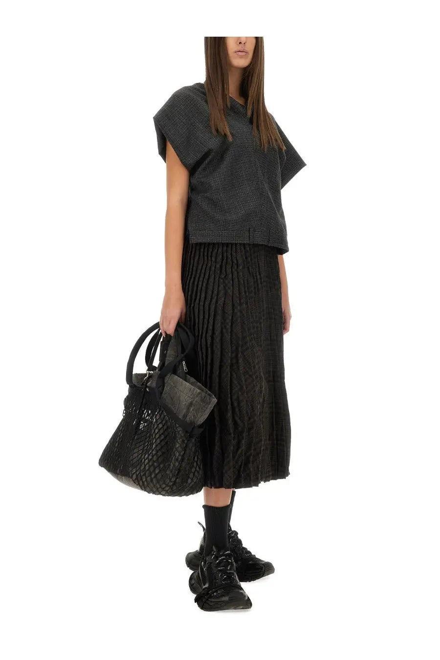 Black textured leather handbag with quilted pattern and top handles accompanying Balenciaga women’s pleated brown skirt