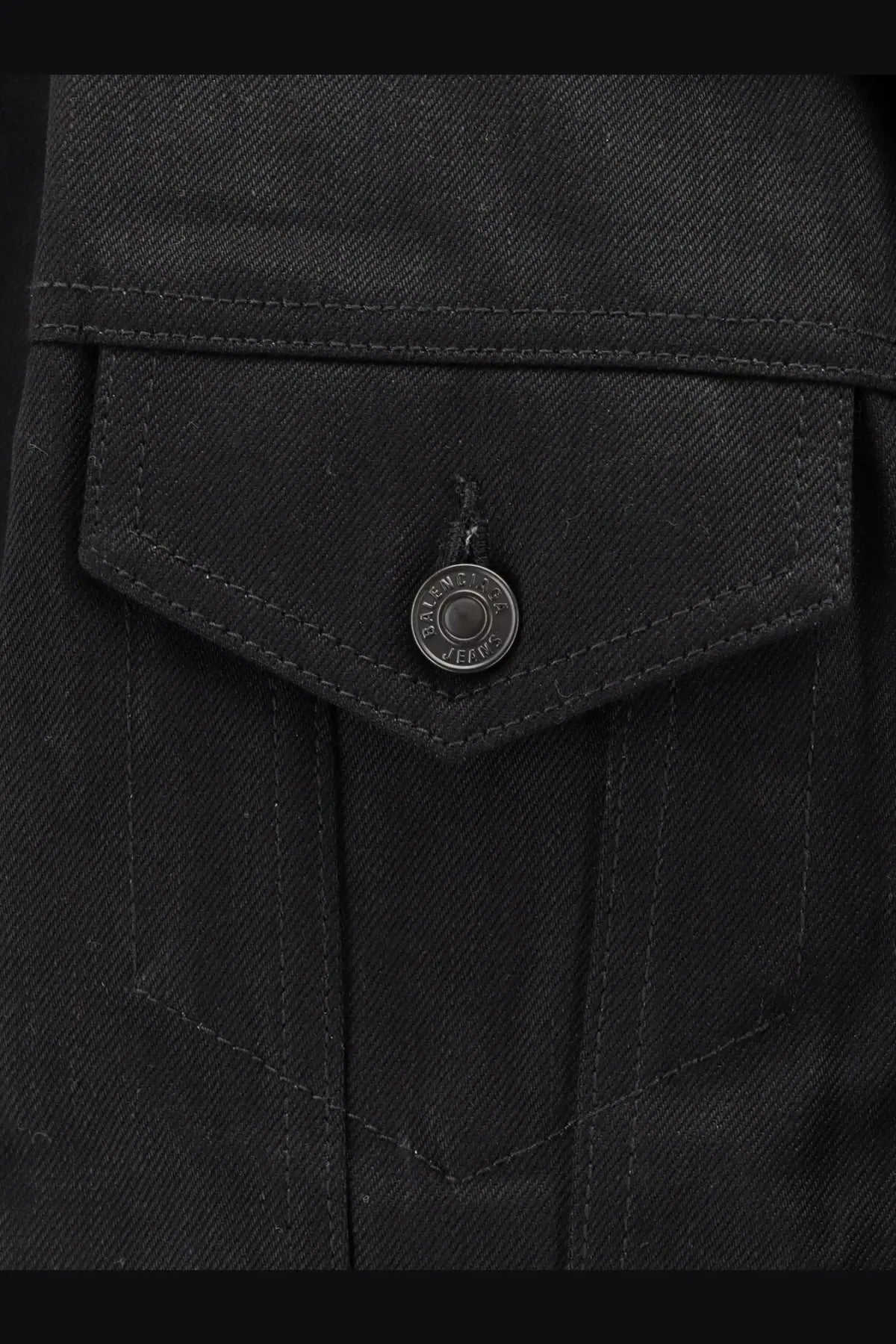 Close up of balenciaga women’s standing black denim jacket pocket with circular metal button engraved with brand text