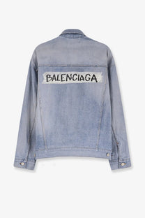 Back of balenciaga women’s washed out light-wash denim jacket with bold black logo and white tape detailing