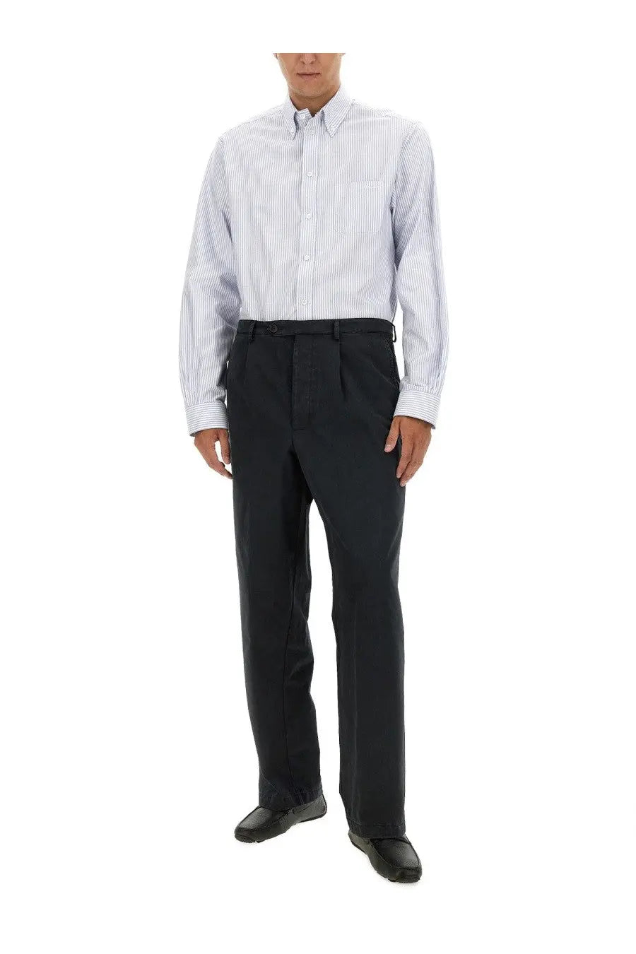 A man wearing Bally men’s black cotton pants paired with a light blue and white striped long-sleeved shirt