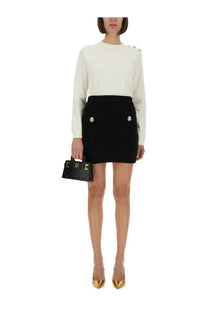 Black textured mini skirt with silver button accents paired with balmain women’s white knitted top front view
