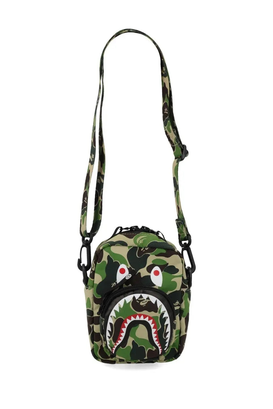A camouflage-patterned bape shark crossbody bag with a bold, stylized shark face design in black and white on the front.