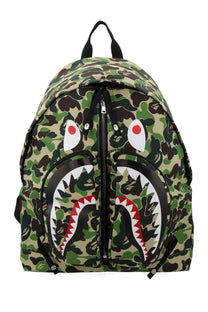 A bathing ape men’s shark green backpack with camouflage pattern and bold stylized shark face with red white teeth accents