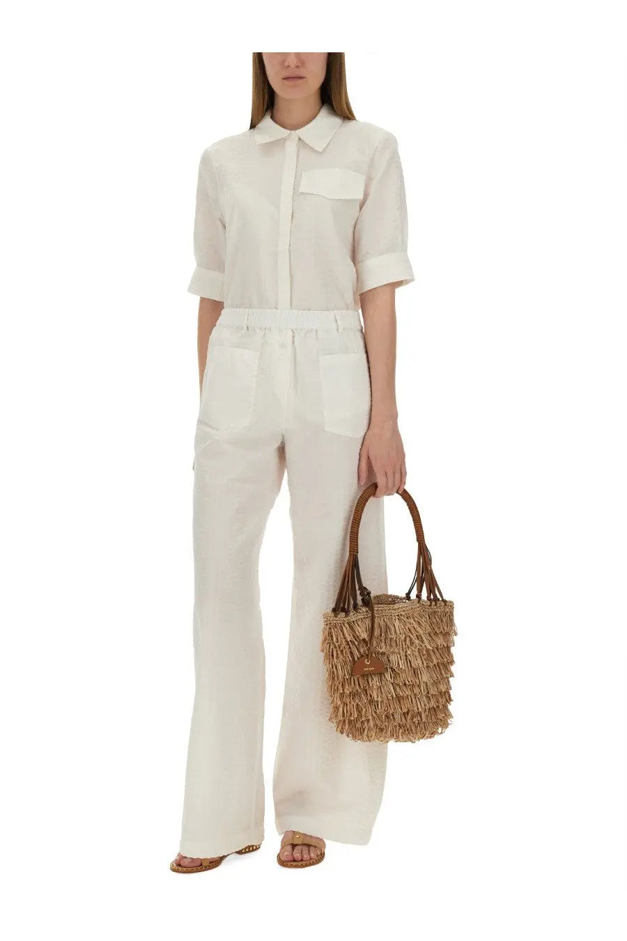A woven straw tote bag with fringed detailing and brown leather handles paired with baum und pferdgarten women’s shirt majken white