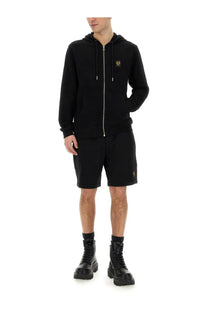 Belstaff men’s black shorts paired with a black zip-up hoodie featuring a gold embroidered logo on the chest