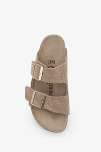 Tan suede birkenstock women’s arizona sandal with two gold-toned buckle straps in beige color